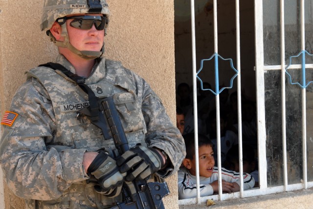 BAGHDAD - Staff Sgt. Daniel McHenry, a Zanesville, Ohio native and cavalry scout squad leader assigned to 1st Squadron, 7th Cavalry Regiment stands near a window as an Iraqi student peers out at his classmates playing in the courtyard here, April...