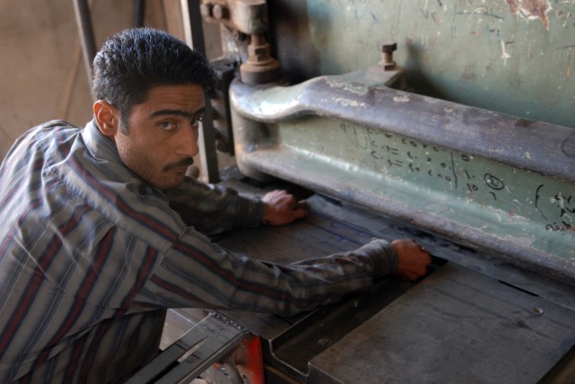 BAGHDAD - An Iraqi factory worker guides a sheet of metal into a machine while 450th Civil Affairs Battalion and embedded Provincial Reconstruction Team members talk with the factory owner and assess his business in Boob al-Sham here, April 14. "We a...