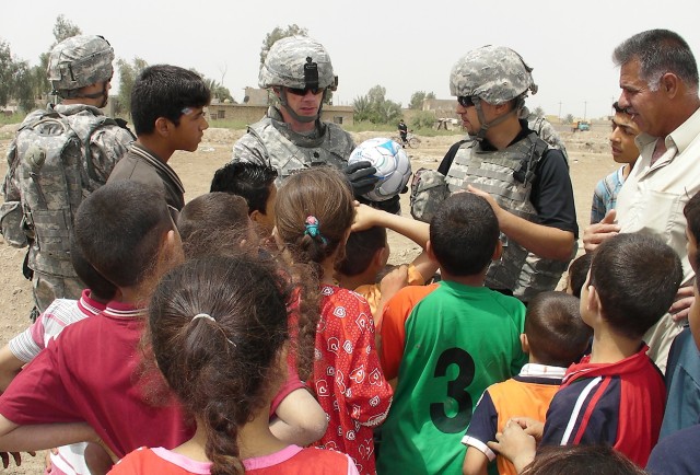 AL-MADAIN, Iraq - Lt. Col. Michael Shinners (center), of Alexandria, Va., shows a group of children a soccer ball with the name Pfc. Nick Madaras written on it while telling them the meaning behind the ball during a site assessment mission April...