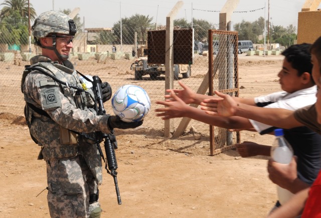 AL-MADAIN, Iraq - 1st Lt. Benjamin Martin, of Sarasota, Fla., prepares to hand a soccer ball to a charging group of Iraqi children during a site assessment mission April 18 in the Al-Madain area of eastern Baghdad. Martin, who serves as the...