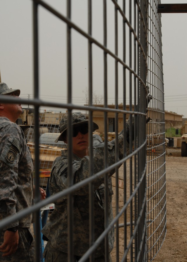 BAGHDAD - Spc. Samantha Schell of Philadelphia holds a piece of wire mesh in place as Sgt. William Funaro of Monroeville, Pa. looks on April 16 at Camp Taji. The Soldiers of the 328th Brigade Support Battalion, 56th Stryker Brigade Combat Team place ...