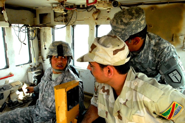 Pfc. Eric Salinas (left), from Victoria, Texas, a heavy equipment operator with the 277th Engineer Company, 46th Eng. Battalion, 225th Eng. Brigade, explains controls and maneuvers in the cab of a bulldozer to his Iraqi Army counterpart through the u...