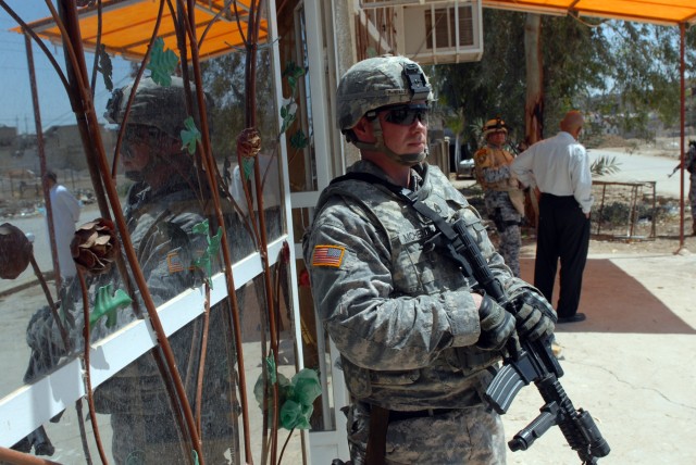 Staff Sgt. Daniel McHenry, a cavalry scout squad leader from Zanesville, Ohio, assigned to Apache Troop, 1st Squadron, 7th Cavalry Regiment, stands guard outside of a shop while his platoon leader discusses a possible micro-grant with the business...