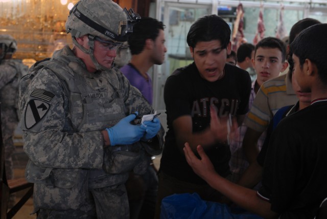 BAGHDAD - Spc. Robert Hamilton, from Corpus Christi, Texas, Company C, 2nd Battalion, 5th Cavalry Regiment, prepares to bandage the thumb of an Iraqi boy in Ula Market in Sadr City, April 19. The boy cut his thumb while preparing meat at a local butc...