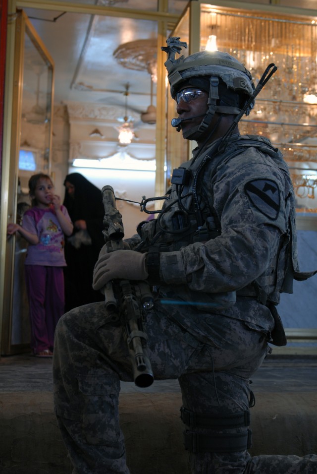 BAGHDAD - Wichita, Kan. native, Cpl. Anthony Jackson, a sniper with Headquarters and Headquarters Company, 2nd Battalion, 5th Cavalry Regiment, takes a knee in front of a gold shop at Ula Market in Sadr City, April 19. The patrol stopped here to asse...