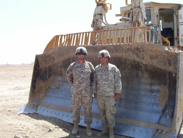 BAGHDAD - Six foot, two inch Ventress, La. Native, Command Sgt. Maj. Joe Major (left,) from the 225th Engineer Brigade, stands in front of the 14-foot wide blade attached to the military D-9 Bulldozer with Pfc. Eric Salinas (right), a member of the 4...