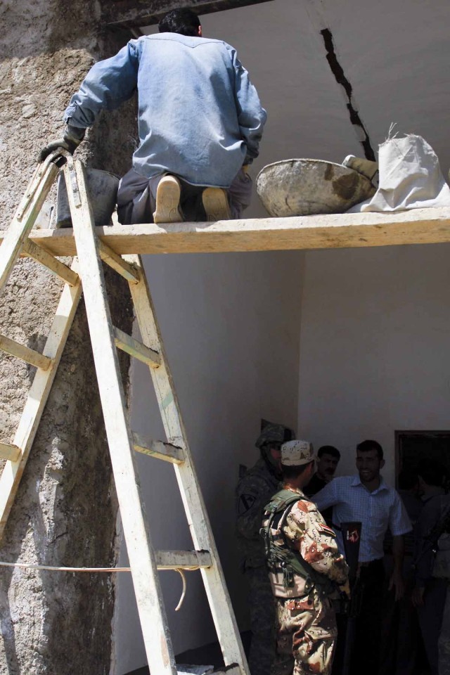 A man works to patch a crack in the roof of the Al Shaheed Hassan School in Muhallabiyah, Iraq while Iraqi Army, Coalition Force and Iraqi Police chat outside one of the school's newly refurbished classrooms. The school's repairs were organized by lo...