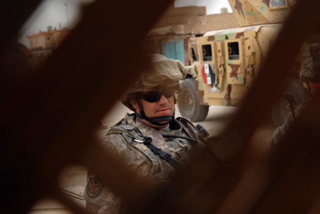 BAGHDAD - Staff Sgt. Marc Paugh, a military policeman from Dunkirk, Ohio, assigned to the 591st MP Company "Spartans," 93rd MP Battalion, 8th MP Brigade, stands guard behind a fence during an opening ceremony for a market opening in Abu Ghraib...