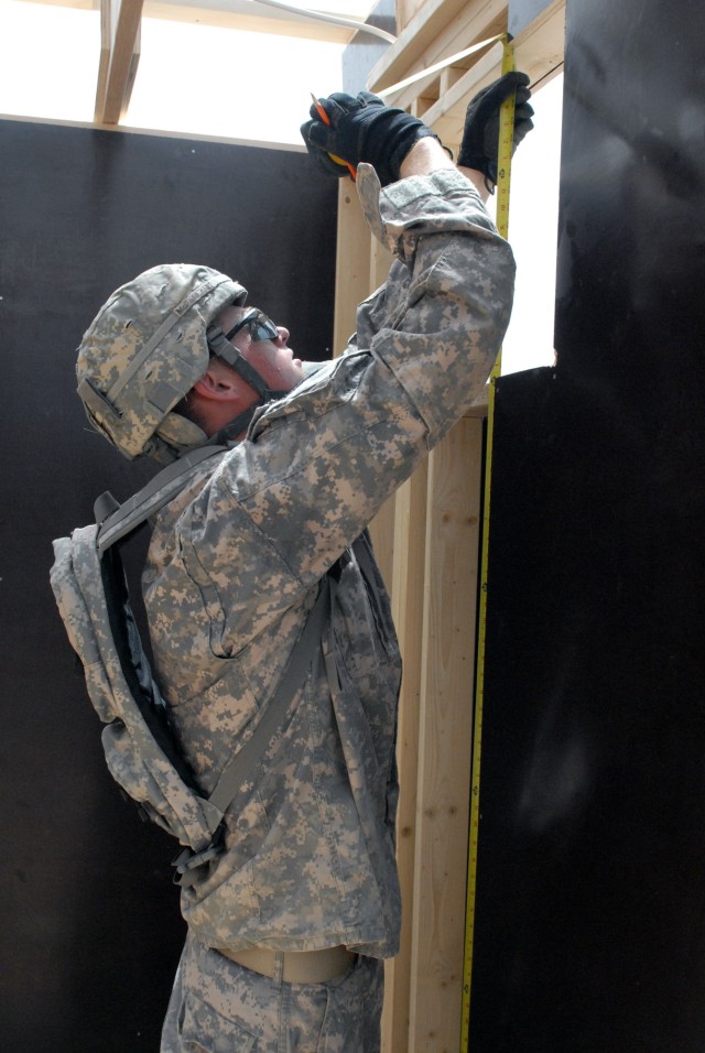 BAGHDAD - Spc. Miles McFarland from Portland, Ore., a member of the 46th Engineer Battalion, 225th Eng. Brigade, 1st Cavalry Division, measures the opening for an environmental control unit before he cuts plywood sheathing for the wall section....