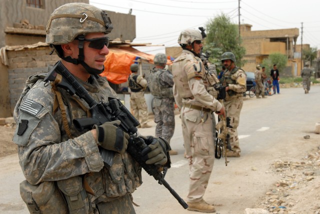 BAGHDAD - Sgt. Matt Coble, a Reedsville, Pa., native and cavalry scout team leader assigned to C Troop, 2nd Squadron, 104th Cavalry Regiment, 56th Stryker Brigade Combat Team, stands guard with an Iraqi Army Soldier while other Soldiers search for...