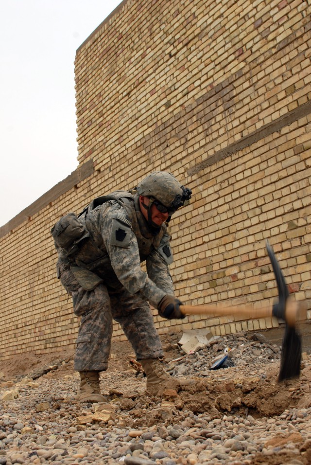 BAGHDAD - Spc. Rodney Maze, a cavalry scout from Washington, Pa., assigned to C Troop, 2nd Squadron, 104th Cavalry Regiment, 56th Stryker Brigade Combat Team, uses a pick axe to clear away hard ground after the "Fido," a portable explosives...