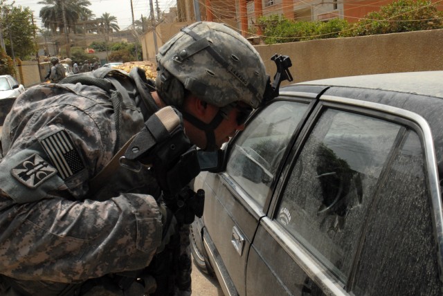 Spc. Christopher Santos of Beckley, W. Va., an artilleryman with 1st Battalion, 7th Artillery Regiment, 2nd Brigade Combat Team, 1st Infantry Division, peers inside a parked vehicle for any illegal items on a street in the Mutanabi neighborhood of...