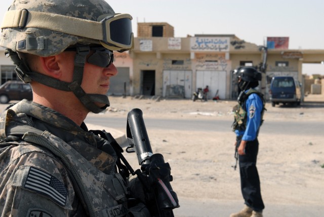 TAJI, Iraq -Cpl. Isaac Hutchison (left), 591st Military Police Company, 93rd MP Battalion, 8th MP Brigade, stays vigilant in the desert heat as Iraqi police conduct a hasty checkpoint to distribute fliers. The Eugene, Ore. native and his platoon...