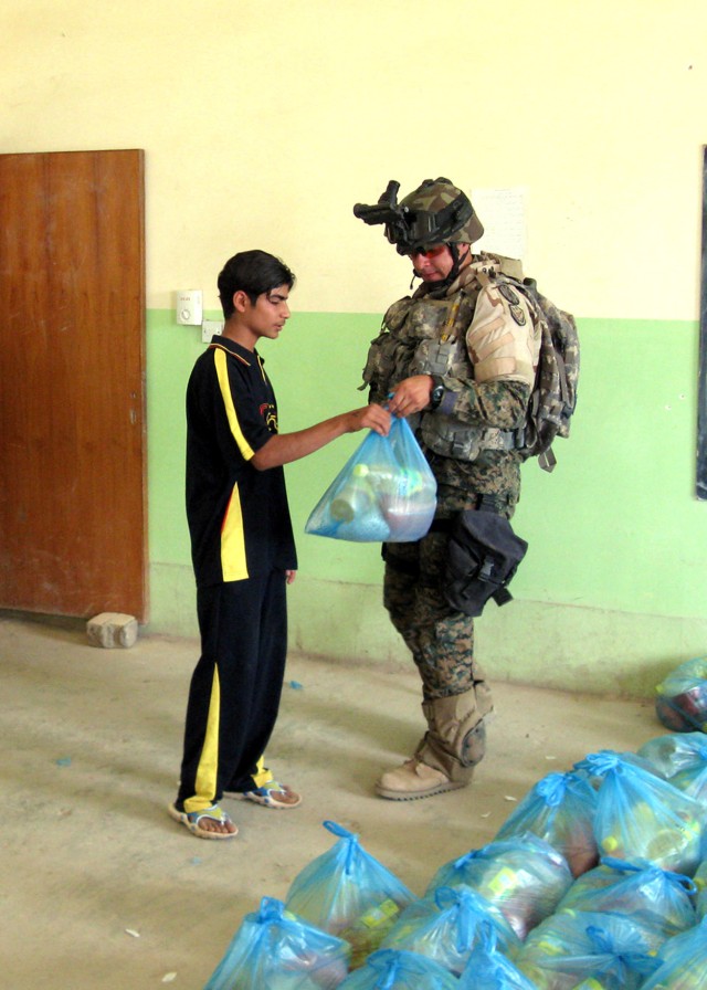 BAGHDAD - An Iraqi Soldier from the 1st Battalion, 24th Brigade, 6th Iraqi Army Division passes out humanitarian aid to a citizen of the Fira Shia area west of Baghdad at the al-Todook Secondary School May 17. Over 100 bags of food were...