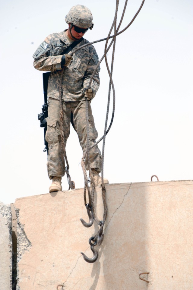 BAGHDAD - Spc. Calob Backes, of Hayden, Colo., assigned to Headquarters and Headquarters Company, Brigade Special Troops Battalion, 3rd Brigade Combat Team, 82nd Airborne Division, stands atop a concrete barrier preparing to hook up cables used to...