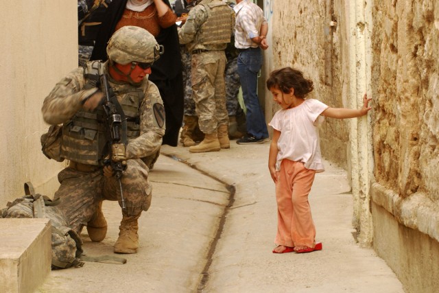 A Soldier with 3rd Battalion, 8th Cavalry Regiment, 3rd Heavy Brigade Combat Team, 1st Cavalry Division demonstrates to an Iraqi child how to properly take a knee on April 23 during Operation Warhorse Scimitar in west Mosul. The child was running...