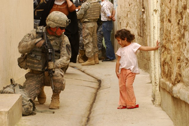 A Soldier with 3rd Battalion, 8th Cavalry Regiment, 3rd Heavy Brigade Combat Team, 1st Cavalry Division demonstrates to an Iraqi child how to properly take a knee on April 23 during Operation Warhorse Scimitar in west Mosul. The child was running up ...