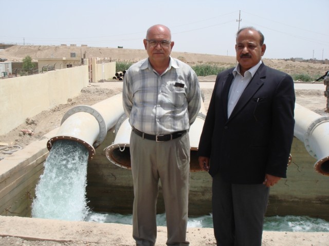 TAJI, Iraq - Engineer Hameed Ibrahim (left), and Directorate General Thair Dahri, both of the Baghdad Water Resources Directorate, stand in front of the irrigation outlet for Pump Station One in Saab Al Bour, Iraq, during a May 16 visit to the...
