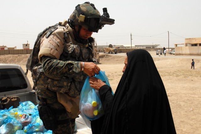BAGHDAD - An Iraqi Soldier based at Joint Security Station Aqur Quf hands out a bag of food to an Iraqi woman at a school in the village of Firra Shia west of Baghdad. "I think it's important for the community to see that the IA and the government...