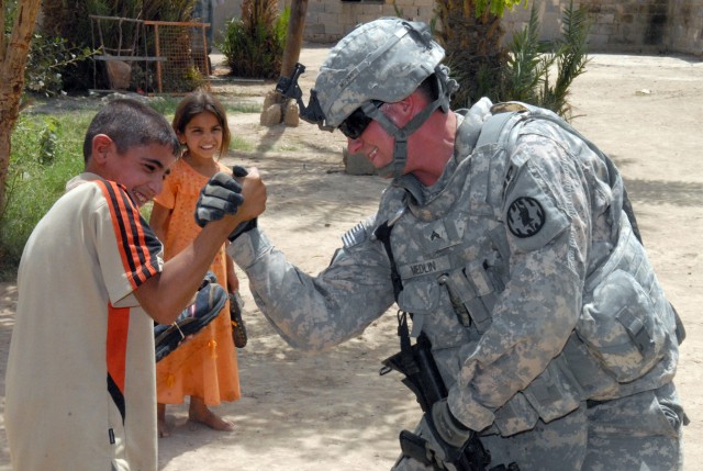 BAGHDAD - Cpl. David Medlin, a native of Buchanan, Mich., a military policeman assigned to the 591st Military Police Company., 93rd MP Battalion, 8th MP Brigade, arm wrestles with a little boy after giving some of the neighborhood children shoes,...