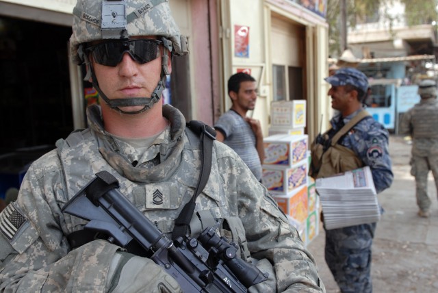 BAGHDAD - Sgt. 1st Class Joseph Bischof, a military policeman and platoon sergeant from Louisville, Ky., assigned to the 300th MP Company, 91st MP Battalion, 8th MP Brigade, stands guard while his Iraqi Police counterpart talks with the locals in...