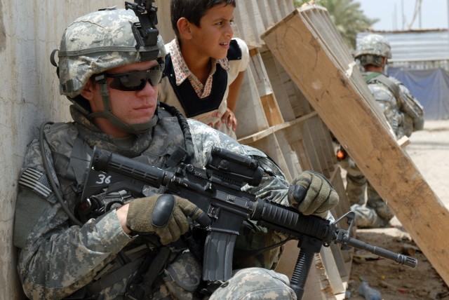 BAGHDAD - Pvt. Justin Smith, a combat medic from Raeford, N.C., assigned to Company B, 2nd Battalion, 5th Cavalry Regiment, 1st Brigade Combat Team, 1st Cavalry Division, takes a knee and pulls security with an Iraqi boy while on patrol in Sadr...