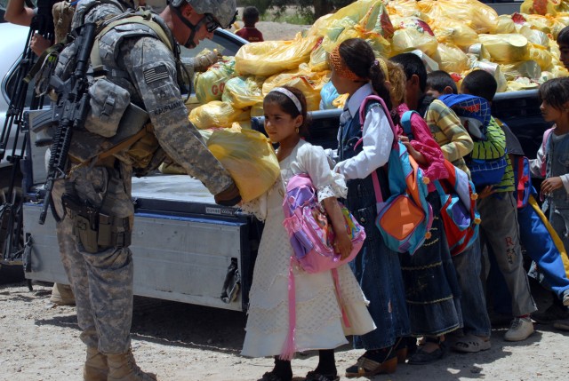 BAGHDAD - Staff Sgt. Brian Kaufman, a native of Marcelous, N.Y. and civil affairs team sergeant assigned to A Company, 403rd Civil Affairs Battalion gives a little girl a bag of food after the ground breaking ceremony at the Zoba Village High...
