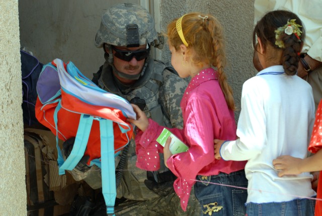 BAGHDAD - Sgt. 1st Class Fredrick Welch, a Montego, N.Y. native assigned to 2nd Battalion, 8th Cavalry Regiment, 1st Cavalry Division, gives a school girl a backpack at the ground breaking ceremony at the Zoba Village High School, June 4.  The...