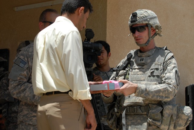 BAGHDAD - Capt. Jeremy Roy (right), a native of Indianapolis and commander of A Company, 2nd Battalion, 8th Cavalry Regiment, 1st Cavalry Division, gives a gift to the headmaster of the Zoba Village High School, June 4.  The school will also...