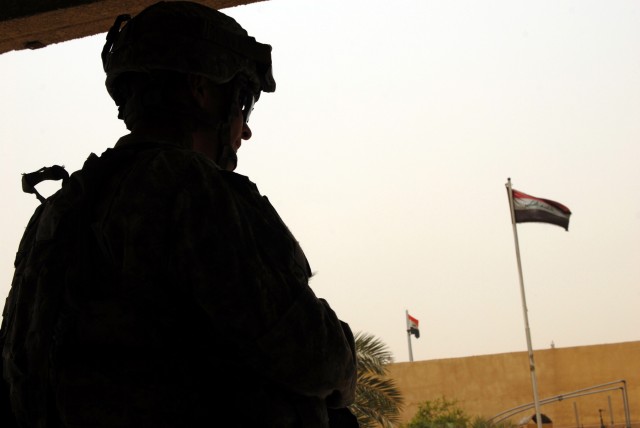 BAGHDAD - Iraqi flags wave in the distance as Greenville, N.C., native, Spc. Jon Stricklin, a squad automatic weapon gunner assigned to A Co., 252nd CAB, 30th HBCT, scans his sector of fire while waiting for his company commander to finish meeting wi...