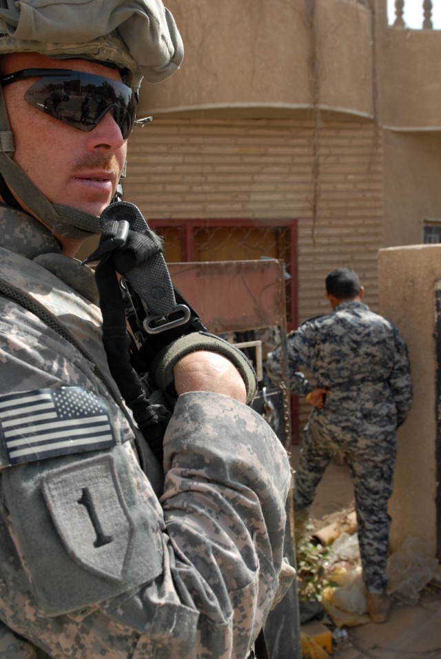 BAGHDAD - An Iraqi National Police officer steps over trash before entering a vacant building to search for weapons caches and explosives as Staff Sgt. Robert Warmack, an infantry squad leader from Cove City, N.C., assigned to Company A, 252nd...