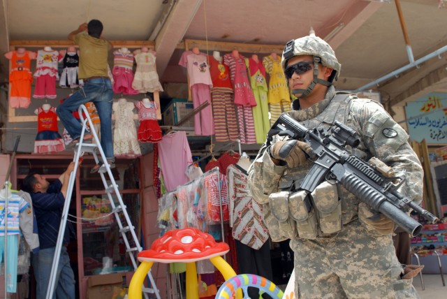 BAGHDAD - Iraqi shopkeepers hang clothes outside a shop in a market in the Doura neighborhood, here, June 11, while Lawrenceville, Ga. native, Spc. Alex Vasquez, an infantryman assigned to Company A, 252nd Combined Arms Battalion, 30th Heavy...