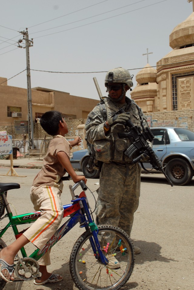 BAGHDAD - Sgt. Reginald Knight, of Gates, N.C., greets an Iraqi boy while walking down a street in a market in the Doura neighborhood here, June 11. Knight pulls security with Company A, 252nd Combined Arms Battalion, 30th Heavy Brigade Combat...