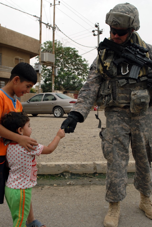 BAGHDAD - Staff Sgt. Robert Warmack of Cove City, N.C., an infantryman assigned to Company A, 252nd Combined Arms Battalion, 30th Heavy Brigade Combat Team, hands out candy to Iraqi children while on patrol in the neighborhood, here, June 12....