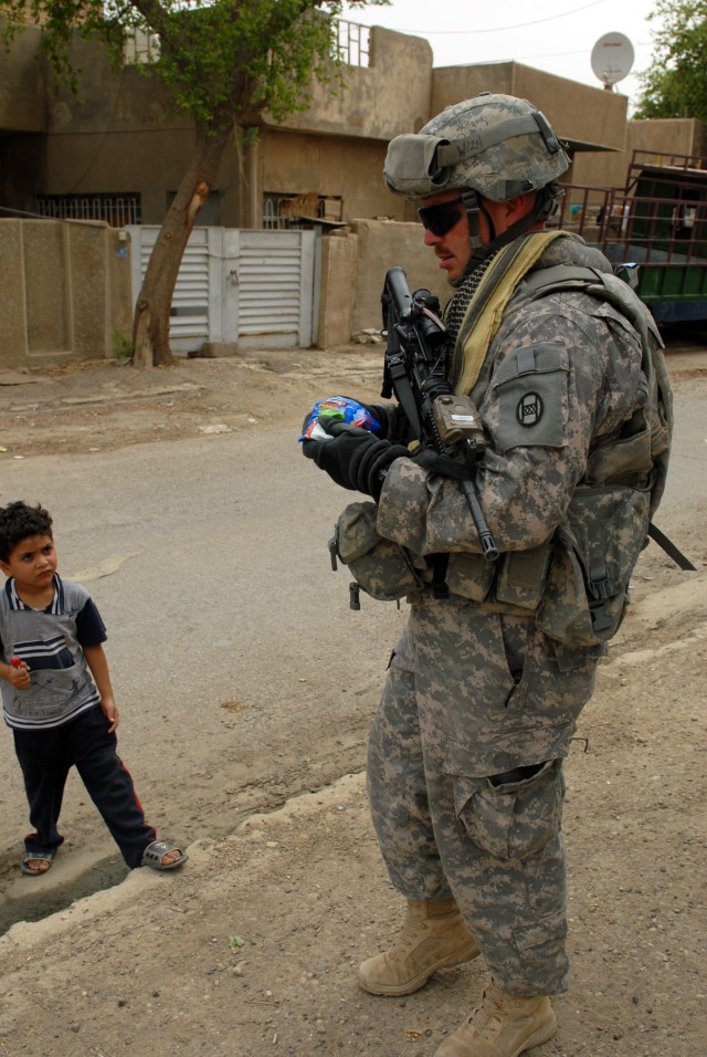BAGHDAD - Staff Sgt. Robert Warmack, an infantryman assigned to Company A, 252nd Combined Arms Battalion, 30th Heavy Brigade Combat Team, hands out candy to an Iraqi child in the Doura neighborhood, here, June 12. Warmack, who is a volunteer...