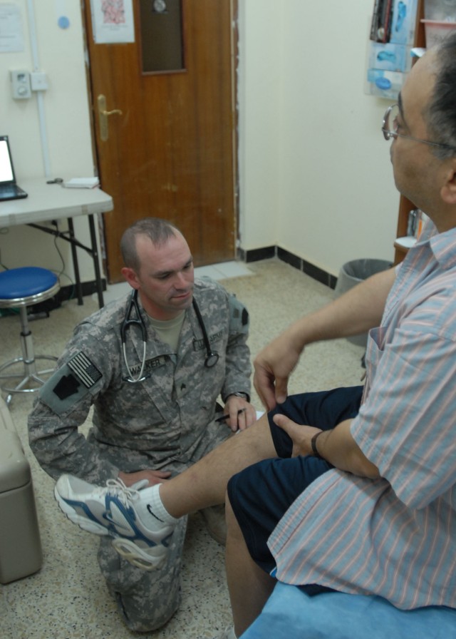 TAJI, Iraq - Sgt. Christopher Walker of York, Pa., a healthcare specialist, with Company C "Charlie Med," 328th Brigade Support Battalion, 56th Stryker Brigade, listens June 13 at Camp Taji, Iraq, north of Baghdad, as a civilian patient talks...
