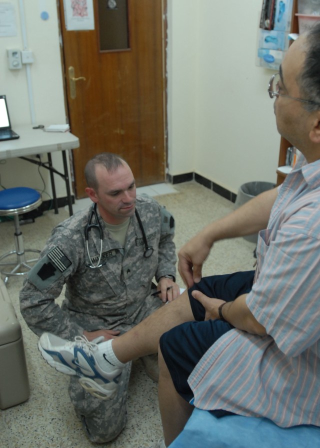 TAJI, Iraq - Sgt. Christopher Walker of York, Pa., a healthcare specialist, with Company C "Charlie Med," 328th Brigade Support Battalion, 56th Stryker Brigade, listens June 13 at Camp Taji, Iraq, north of Baghdad, as a civilian patient talks about k...