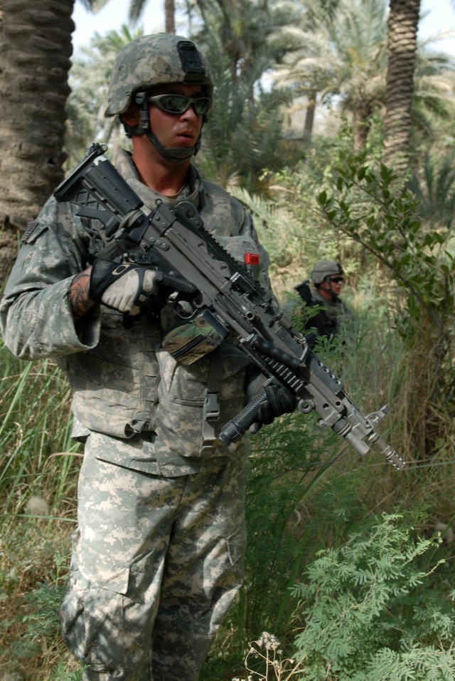 BAGHDAD - Pvt. Jason Kruger of Kitty Hawk, N.C, (left) and Pfc. Gary Hill of Gastonia, N.C., both M-249 Squad Automatic Weapon gunners, pull security in a palm grove during a weapons cache search with the Iraqi National Police near Doura, here,...