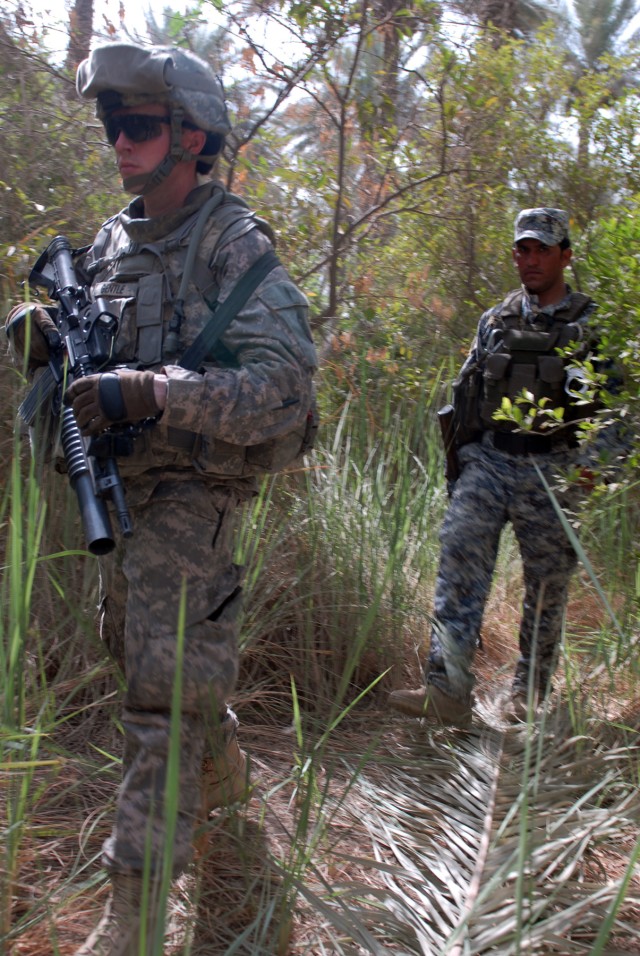 BAGHDAD - Pfc. Daniel Gentle of Winston-Salem, N.C., leads an Iraqi National policeman through a palm grove in Doura, here, June 13. Gentle, an infantryman assigned to Company A, 252nd Combined Arms Battalion, 30th Heavy Brigade Combat Team, was...