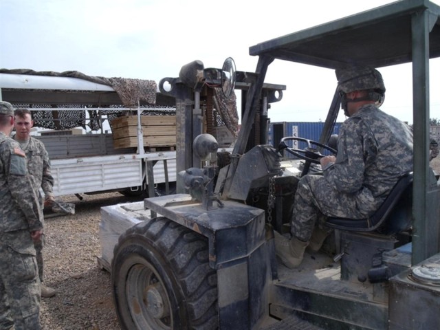 Sgt. Marcus McDowell, a native of Helena, Mont., with the 639th Quartermaster Company loads a pallet of cinderblocks under the watchful eye of an Iraqi Police commander at Camp Vic