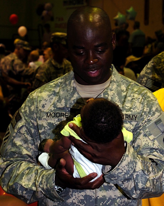 Master Sgt. Eric Moore, maintenance control sergeant, 602nd Maintenance Company, 49th Transportation Battalion, 15th Sustainment Brigade, 13th Sustainment Command (Expeditionary), holds his grandson for the first time at a redeployment ceremony at...