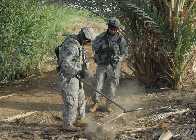 NUBAI, Iraq - Pfc. Darryl Strickland (left), of Philadelphia and Staff Sgt. Joshua Bentley of York, Pa. investigate a "beep" from a metal detector as Strickland runs it across a pile of debris June 16 near Nubai, north of Baghdad. The Soldiers are...