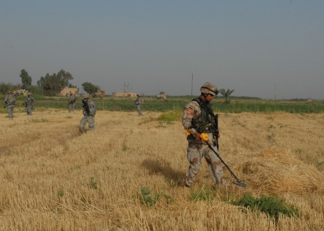 NUBAI, Iraq - An Iraqi Army Soldier uses a metal detector to search a pile of loose straw June 16 during an IA-led effort to search for weapons caches near Nubai, north of Baghdad. Pennsylvania Army National Guard Soldiers from 1st Battalion,...