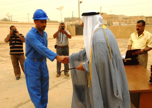 CAMP TAJI, Iraq -Sheikh Saed Jassim (right) presents a diploma to a new graduate of the Ministry of Electricity's Electrical Line Refurbishment Team class in Tarmiyah, June 18.  Twenty students graduated the six-week class which gave them skills...