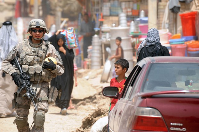 BAGHDAD - An Iraqi boy looks on as Spc. Carlin Redhouse, of Kirtland, N.M. holds a ball as he walks the streets of the Baghdad suburb of Oubaidy during a foot patrol June 21 in the 9 Nissan district of eastern Baghdad. The combined patrol was to...