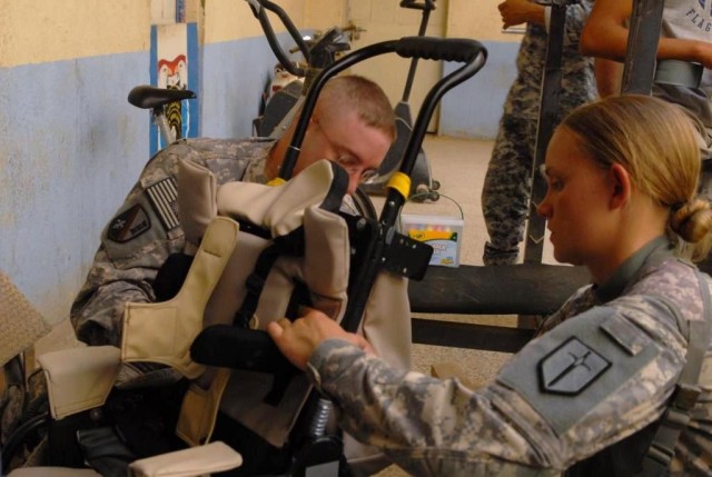 BAGHDAD -225th Engineer Brigade Soldiers, Sgt. Maj. Timothy Adam (left), of Pineville, La., and Spc. Jacoba Vermeulen (right), a medic from Phoenix, Ariz., work to adjust a wheelchair for a disabled child, June 20, at  Joint Security Station...