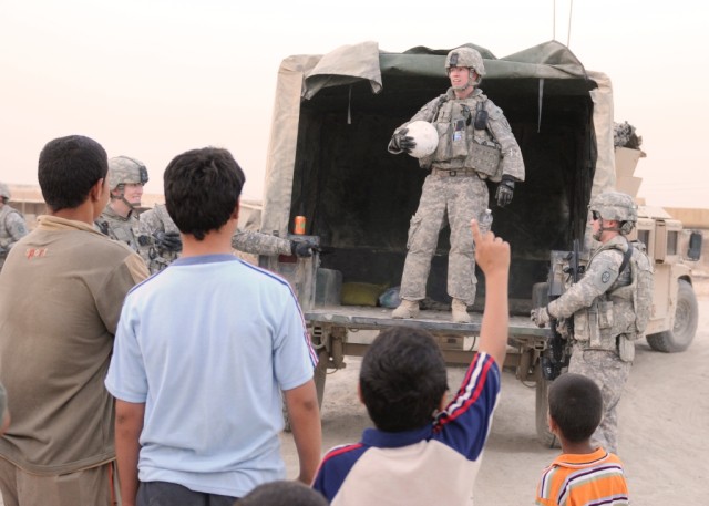 BAGHDAD- Capt. Sara Woods (standing in humvee), of Janesville, Minn., prepares to throw a soccer ball to a group of children, June 22, in a village just outside of Forward Operating Base Mahmudiyah. Woods, part of Civil Affairs Team 31, 120th Combine...