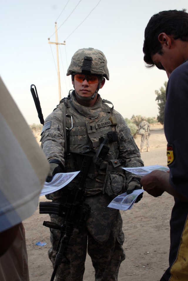 BAGHDAD - 1st Lt. Kevin Mussman, a tank officer assigned to Company D, 1st Battalion, 63rd Combined Arms Battalion, 2nd Brigade Combat Team, 1st Infantry Division, hands out pamphlets to Iraqis in the Khadir village, in the Abu Ghuraib area here, Jun...