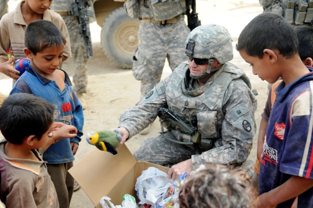 MAHMUDIYAH, Iraq - Command Sgt. Maj. Russell Prince, 120th Combined Arms Battalion, 30th Heavy Brigade Combat Team, of Sneads Ferry, N.C., hands out toys to children on a dairy farm south of Baghdad, June 23.  Soldiers with the 120th Combined Arms Ba...