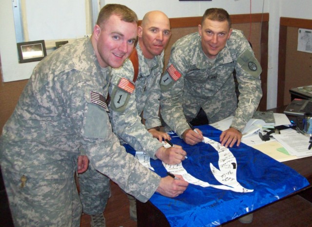 BAGHDAD - From left, First Lt. Ryan Wolfe, 1st Sgt. Elmer Harmond and Capt. Mark Houck of A Troop, 150th Armored Reconnaissance Squadron, sign thank you messages on the Mountain State University banner at Camp Stryker June 25.   Soldiers from the...